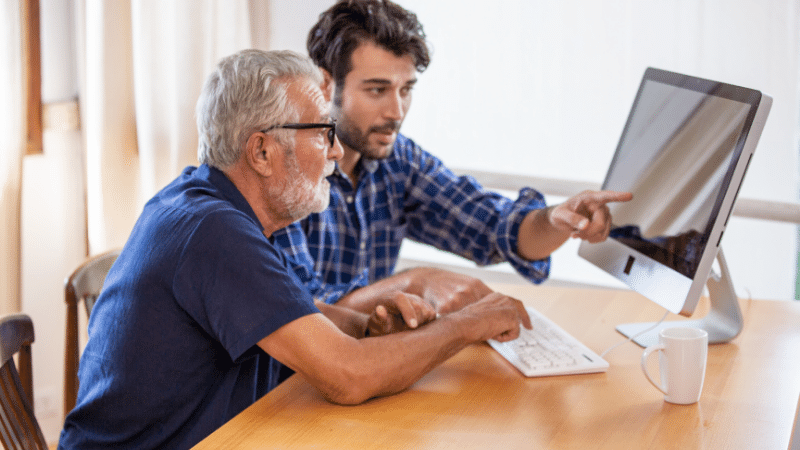 A son is helping his senior father with something on computer